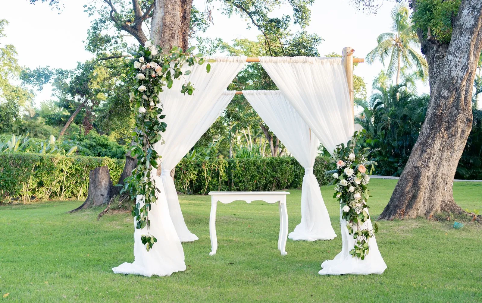 Beautifully decorated outdoor wedding arch with floral arrangements in a lush garden.